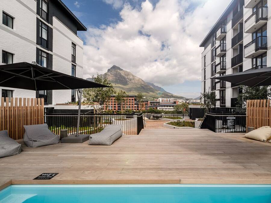 Zona de piscina en la azotea con vista a la montaña, terraza de madera y edificios modernos.