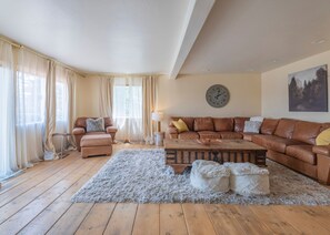 A living room with a brown leather sofa, a wooden coffee table, a fluffy rug, and a wall clock. - Iconic Lakeview Estate | 4BR | Sleeps 10 (Lake Arrowhead)