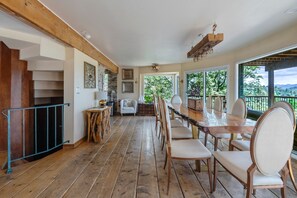 A spacious dining area with a long wooden table, multiple chairs, and a view of the outdoors. - Iconic Lakeview Estate | 4BR | Sleeps 10 (Lake Arrowhead)