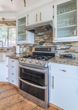 A kitchen with white cabinets, a stainless steel stove, and a stone backsplash. - Iconic Lakeview Estate | 4BR | Sleeps 10 (Lake Arrowhead)