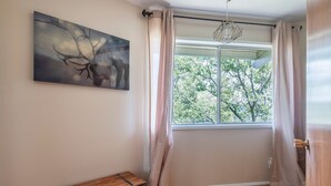 A room with a large window, a wooden chest, and a painting of a deer. - Iconic Lakeview Estate | 4BR | Sleeps 10 (Lake Arrowhead)