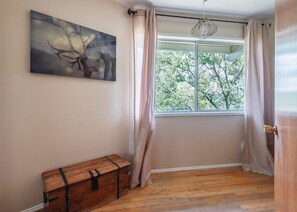 A room with a large window, a wooden chest, and a painting of a deer. - Iconic Lakeview Estate | 4BR | Sleeps 10 (Lake Arrowhead)