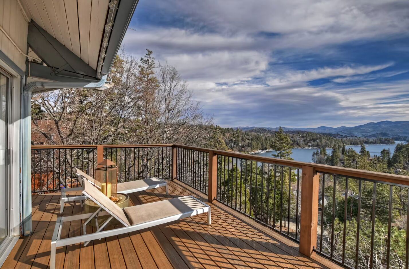 Une terrasse en bois avec deux chaises longues, une table et une rambarde d’où l’on peut admirer un lac et des montagnes boisées.