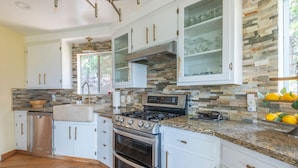 A modern kitchen with granite countertops, stainless steel appliances, and a stone backsplash. - Iconic Lakeview Estate | 4BR | Sleeps 10 (Lake Arrowhead)