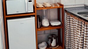 Eine Küche mit Mikrowelle, Kühlschrank, Regalen mit Geschirr, einem Mixer und einer Topfpflanze.