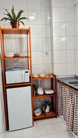 A kitchen with a microwave, refrigerator, shelves with dishes, a blender, and a potted plant. - Charming Apartment in the Heart of Belém, Amazon (Belém)