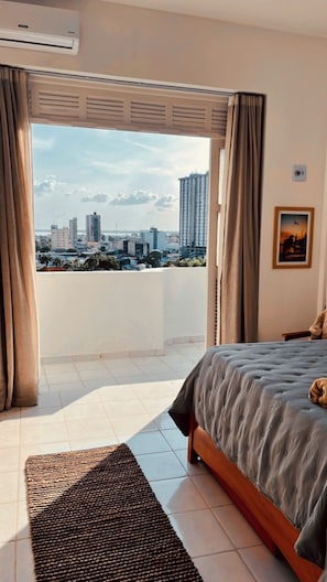 Quarto com cama, vista da cidade e janela com cortinas.
