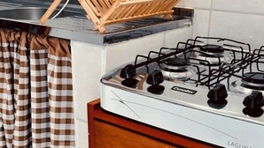 Eine Küche mit Gaskochfeld, Wäscheständer aus Holz und karierten Vorhängen.