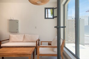 A room with a wooden table, two white sofas, a wicker ceiling light, a window with a view of a fence, and a wall-mounted electrical box. - Born | Modern 2BR with Pools and Gym (Bavaro)