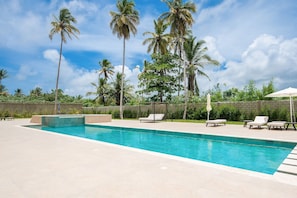 A swimming pool with lounge chairs, palm trees, and a clear sky. - Born | Modern 2BR with Pools and Gym (Bavaro)