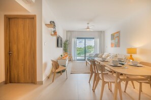 A modern dining area with a wooden table and chairs, a ceiling fan, and a view through the glass door. - Born | Modern 2BR with Pools and Gym (Bavaro)