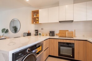 A modern kitchen with a built-in washing machine, a coffee maker, and a microwave. - Born | Modern 2BR with Pools and Gym (Bavaro)