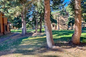 A courtyard with trees and a building with a beige exterior. - Cozy Mammoth Condo | Hot Tub & Mountain Adventure (Mammoth Lakes)