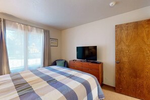 Ein Hotelzimmer mit Bett, Fernseher auf einer Holzkommode, einer Tür und einem Fenster mit Vorhängen.