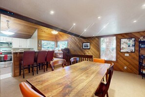 Un coin repas avec une table et des chaises en bois, une cuisine avec des meubles blancs et une grande fenêtre donnant sur un beau paysage.