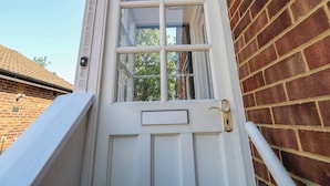 A white door with a brass handle and a small mail slot, set in a brick wall. - Sussex Close (New Malden)
