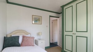 A bedroom with a bed, pillows, a nightstand, a lamp, a door, and a framed picture on the wall. - Sussex Close (New Malden)