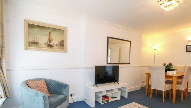 A living room with a sofa, TV, dining table, chairs, a mirror, and a painting on the wall. - Sussex Close (New Malden)