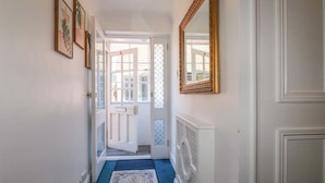A hallway with a blue carpet, a white door, a white radiator, and a gold-framed mirror. - Sussex Close (New Malden)