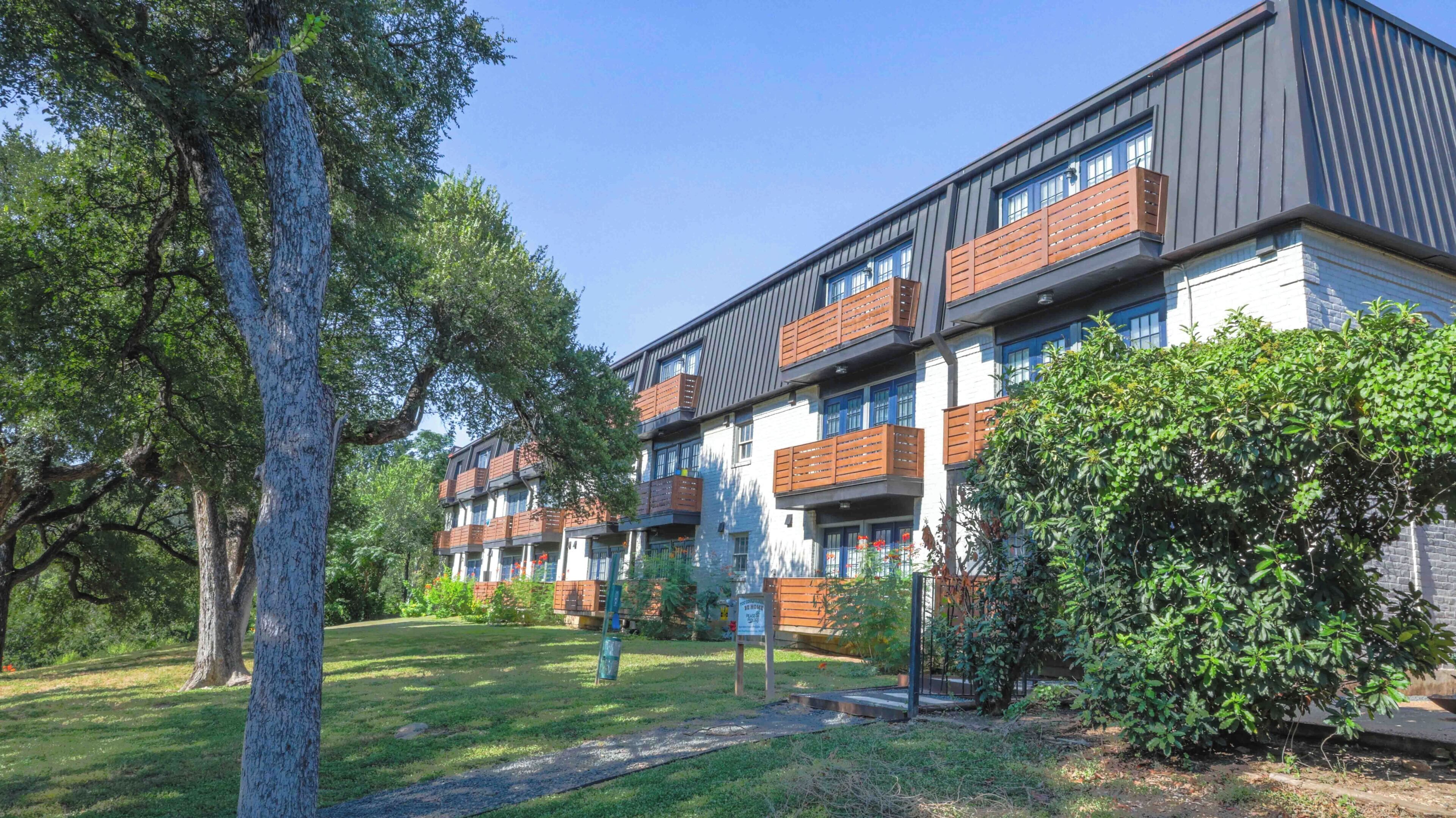 Un immeuble résidentiel à plusieurs étages, doté de balcons et entouré de verdure et d’arbres.
