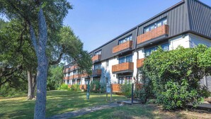 Un edifici residencial de diverses plantes amb balcons, envoltat de verdura i arbres.