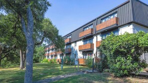 Un immeuble résidentiel à plusieurs étages, doté de balcons et entouré de verdure et d’arbres.