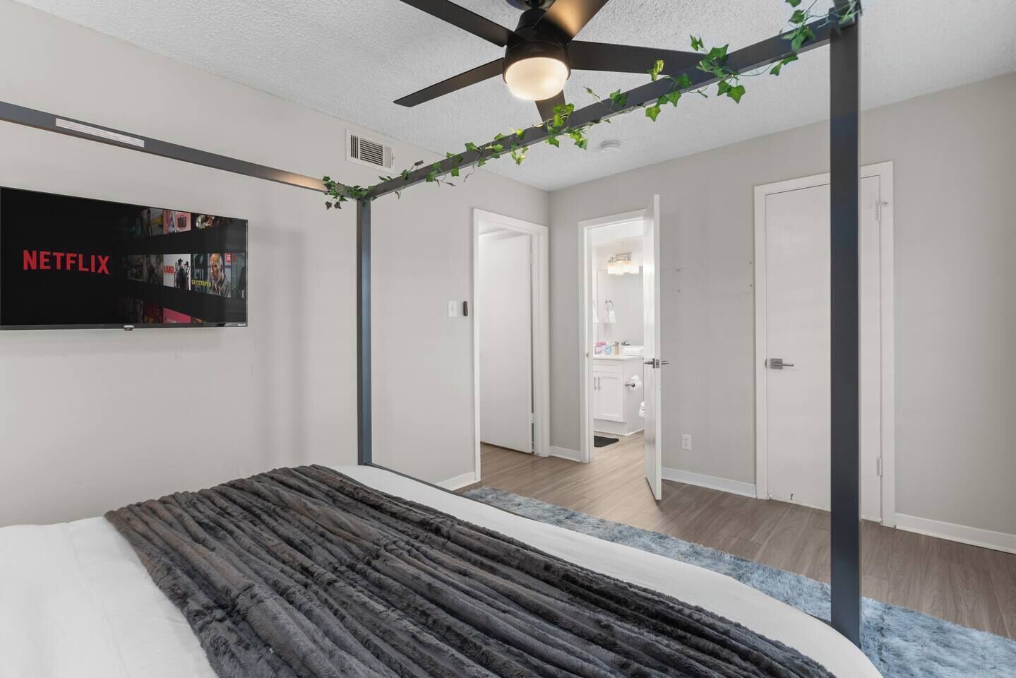 A bedroom with a bed, a ceiling fan, a TV, and a door leading to a bathroom.