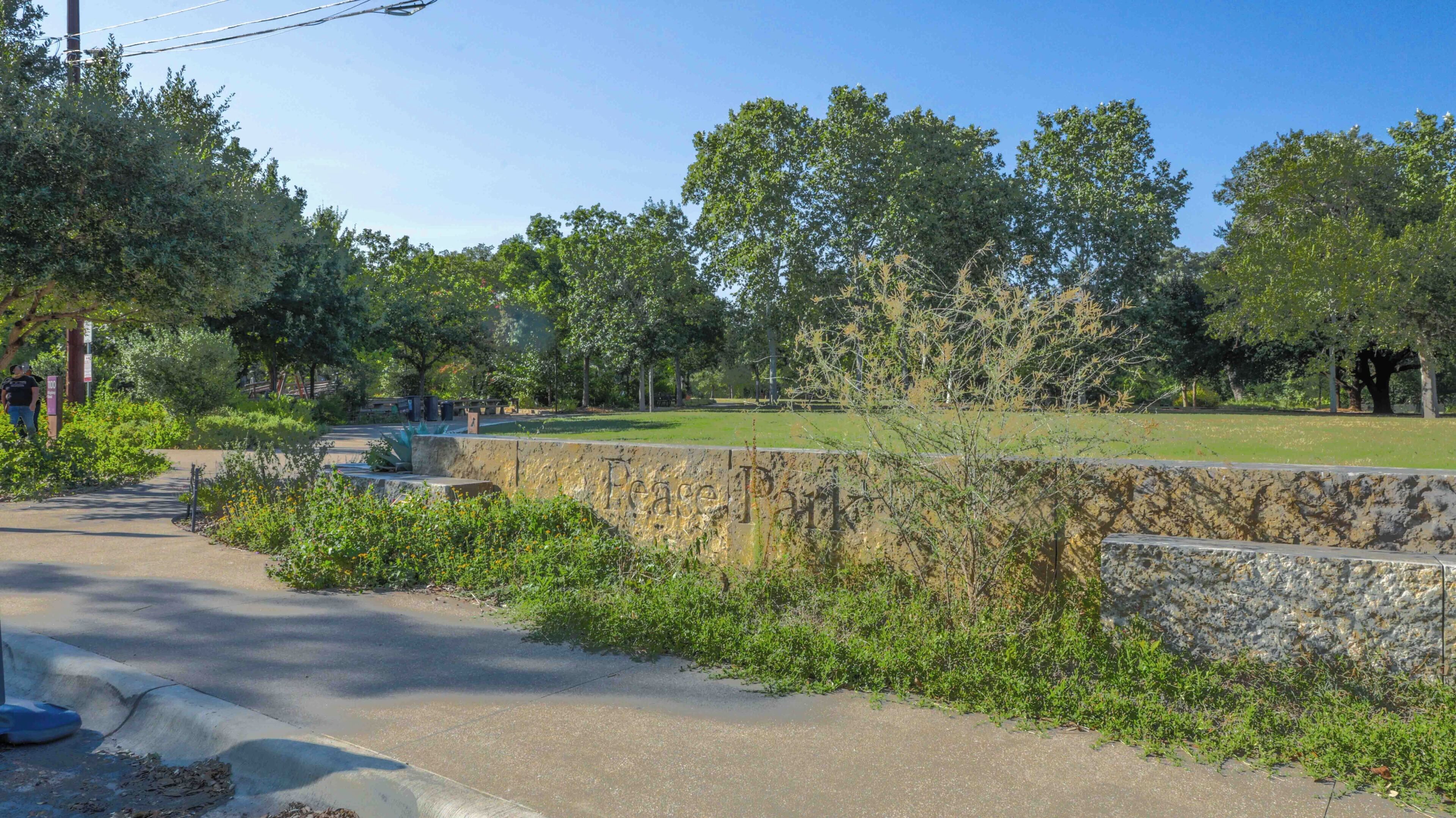 Un chemin pavé longe un mur de pierres, avec de la verdure et des arbres en arrière-plan.