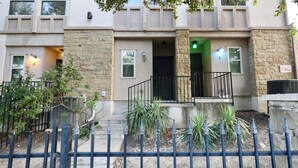 Un immeuble résidentiel à plusieurs étages, doté d’une façade en pierre, de portes numérotées et d’une entrée fermée par un portail.