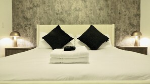 Habitación de hotel con una cama, dos almohadas negras, una toalla blanca y dos lámparas de noche.