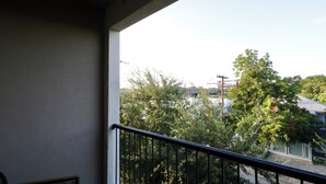 Un balcon doté d’une rambarde en métal, donnant sur un quartier résidentiel avec des arbres et un immeuble sur lequel on aperçoit une grue.
