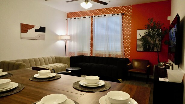 Un coin repas avec une table en bois dressée pour quatre personnes, un canapé et un téléviseur.