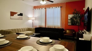 Een eetgedeelte met een houten tafel voor vier personen, een bank en een televisie.