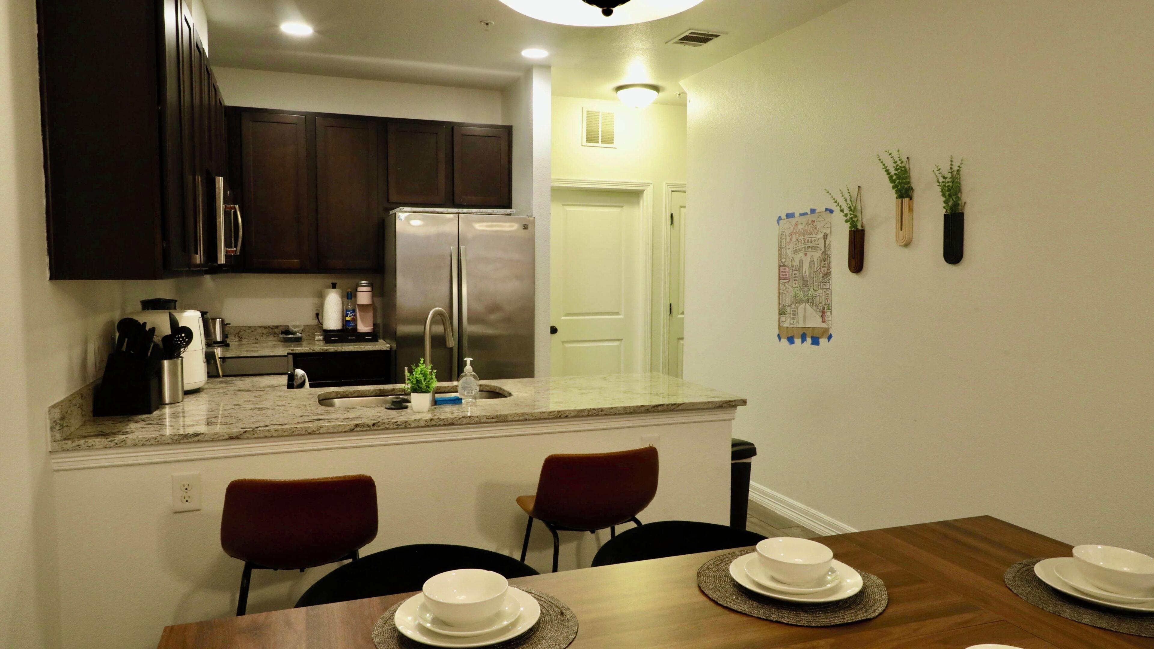 A modern kitchen with dark cabinets, a stainless steel refrigerator, and a dining area with a wooden table and chairs.