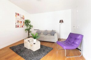 Ein Wohnzimmer mit einer Couch, einem violetten Sessel, einer Pflanze, einem Couchtisch und einer Lampe.