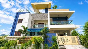 A modern multi-story house with a balcony, a staircase, and a gated entrance.