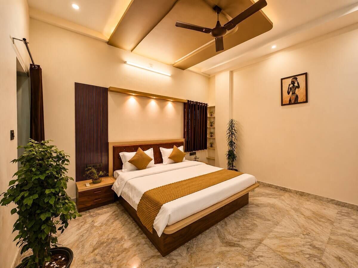 Une chambre d’hôtel avec un grand lit, un ventilateur de plafond, une table de chevet, une plante en pot et une œuvre d’art accrochée au mur.