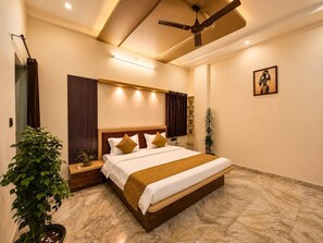 Une chambre d’hôtel avec un grand lit, un ventilateur de plafond, une table de chevet, une plante en pot et une œuvre d’art accrochée au mur.
