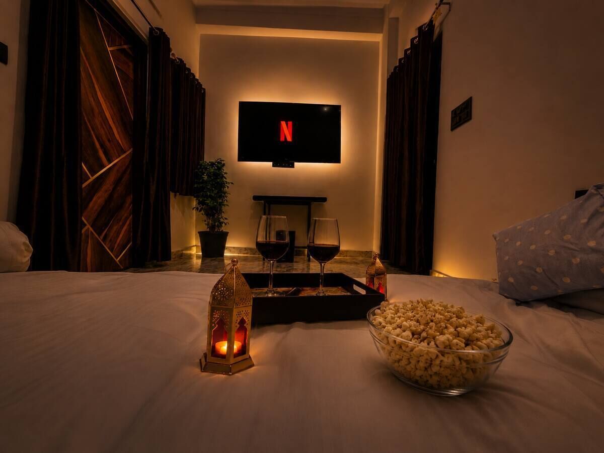 A hotel room with a bed, a TV mounted on the wall, a tray with glasses and a bottle, a bowl of popcorn, and a lit candle.