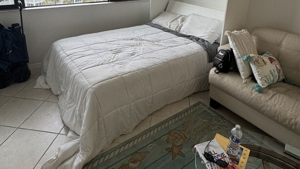A bedroom with a bed, a sofa, a window with a view of buildings, and a tiled floor. - HAPPY PLACE! Charming condo in marvelous Siesta Key perfect for your getaway (Siesta Key)