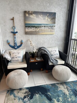 A cozy seating area with a wicker sofa, two poufs, a small table, and a wall-mounted anchor decoration. - HAPPY PLACE! Charming condo in marvelous Siesta Key perfect for your getaway (Siesta Key)