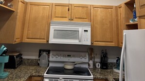 A kitchen with wooden cabinets, a white microwave, a stove, and a ceiling fan. - HAPPY PLACE! Charming condo in marvelous Siesta Key perfect for your getaway (Siesta Key)