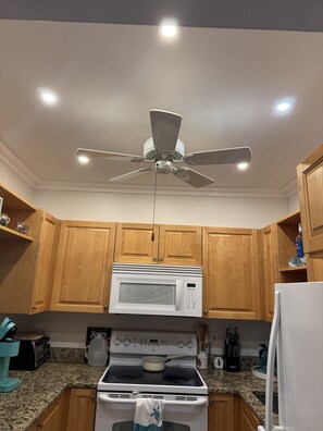 A kitchen with wooden cabinets, a white microwave, a stove, and a ceiling fan. - HAPPY PLACE! Charming condo in marvelous Siesta Key perfect for your getaway (Siesta Key)