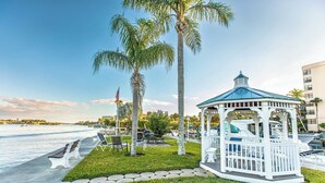 A gazebo with a blue roof, surrounded by a well-maintained lawn and palm trees, overlooking a marina with boats. - HAPPY PLACE! Charming condo in marvelous Siesta Key perfect for your getaway (Siesta Key)