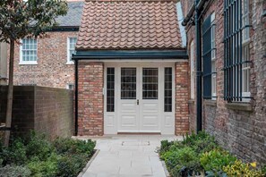 Une maison en briques avec un toit en tuiles, une porte d’entrée blanche et un petit jardin.