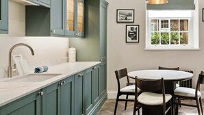 Una cucina con mobili color petrolio, un piano di lavoro bianco e un'area pranzo con un tavolo rotondo e sedie.
