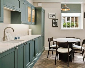 A kitchen with teal cabinets, a white countertop, and a dining area with a round table and chairs. - Preacher's Yard Stylish Central York Apartment - Courtyard 1 (York)