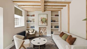 Un soggiorno con travi a vista in legno, un caminetto, un divano, una poltrona e mensole piene di libri.