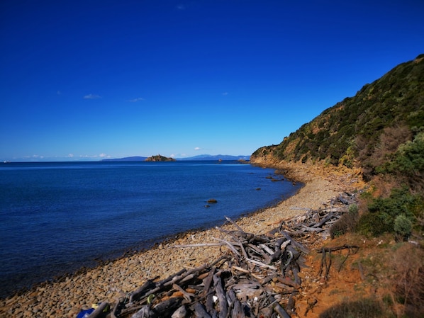A coastal landscape with a rocky beach, calm sea, and distant mountains.
