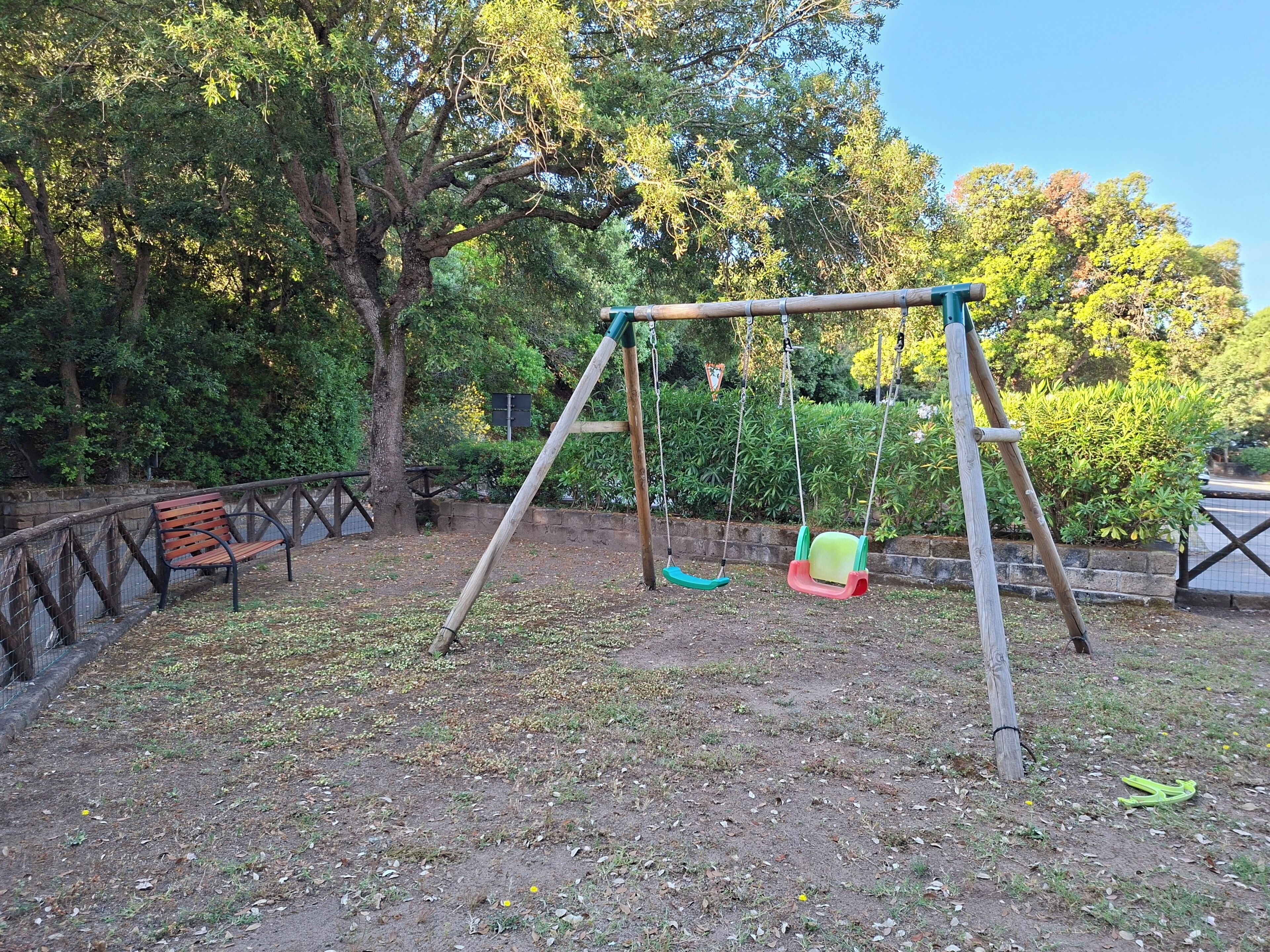 A swing set in a park with a bench and trees in the background.